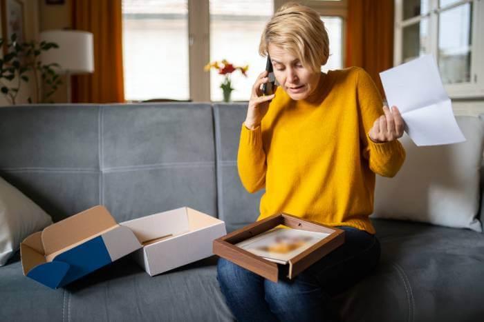 Frustrated woman talking on phone and looking at a damaged purchase.