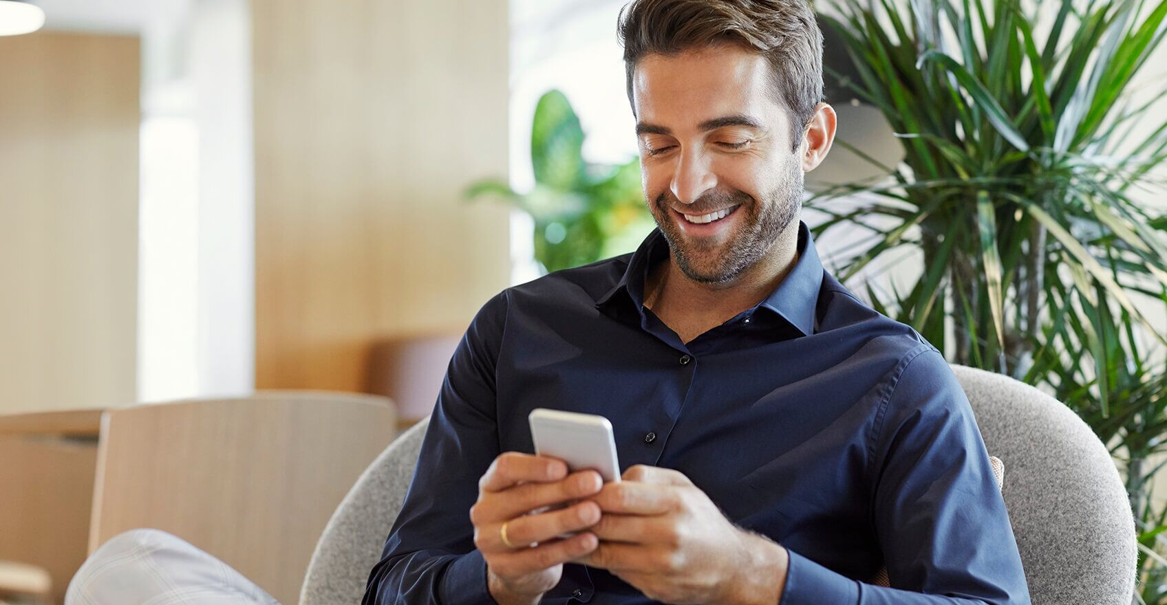 Hombre sonriendo mientras escribe por teléfono.