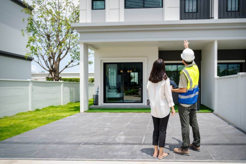 Woman homeowners talking to a home inspector as they look up at the house from outdoors.