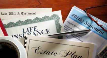 Estate planning documents including a Last Will and Testament, estate plan, life insurance policy and 401(k) statement laying on a desk with an ink pen and cup of coffee.