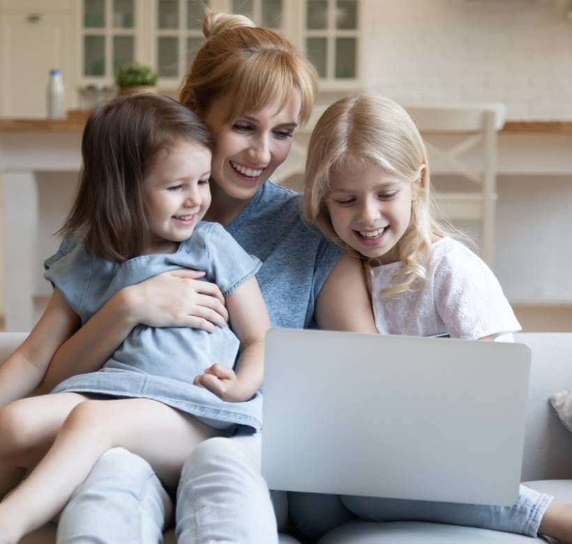 Una madre sonriente y sus dos hijas pequeñas mirando la pantalla de un ordenador portátil.