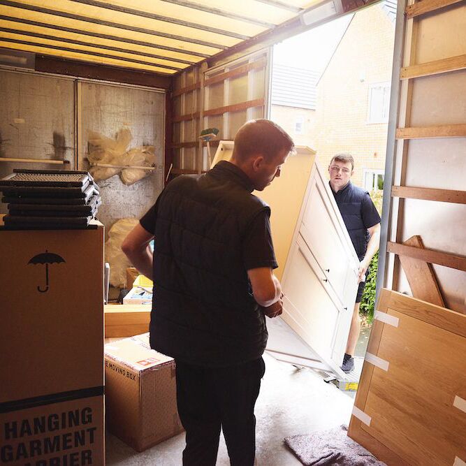 Hombres trasladando un armario alto dentro o fuera de un garaje que contenga cajas de mudanza.