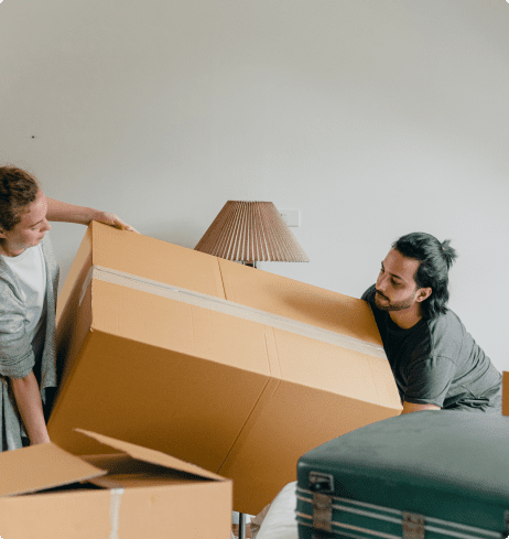 Un hombre y una mujer levantan una gran caja de mudanza en el salón de su casa.