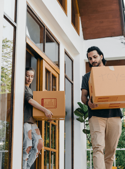 Un hombre y una mujer sacan cajas de mudanza por la puerta principal de su vivienda de alquiler.