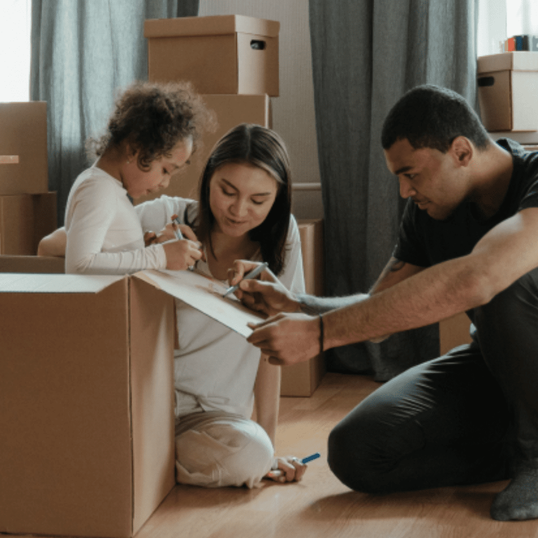 Niño pequeño, madre y padre escribiendo en cajas de mudanza en su salón.