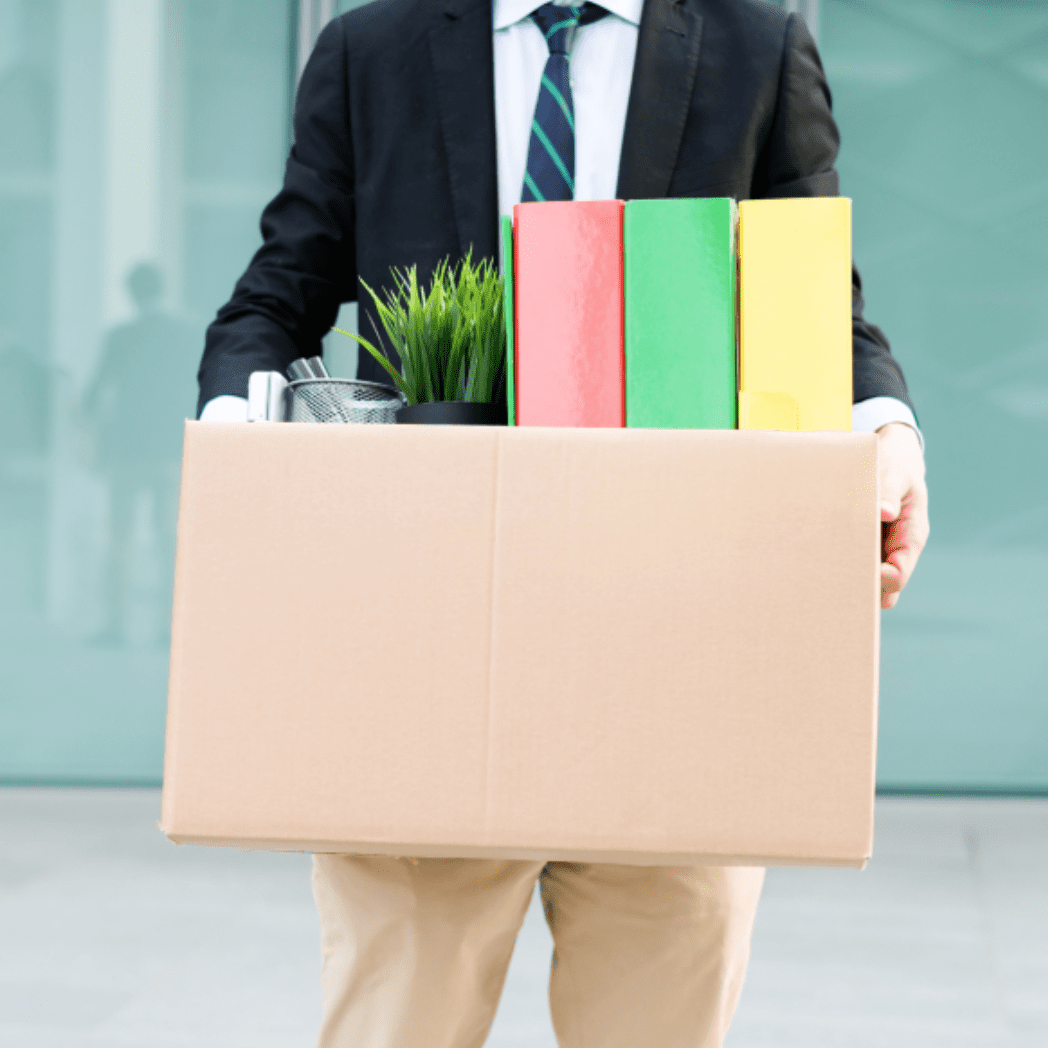 Un hombre con traje de negocios lleva sus pertenencias en una caja marrón tras ser despedido de su trabajo.