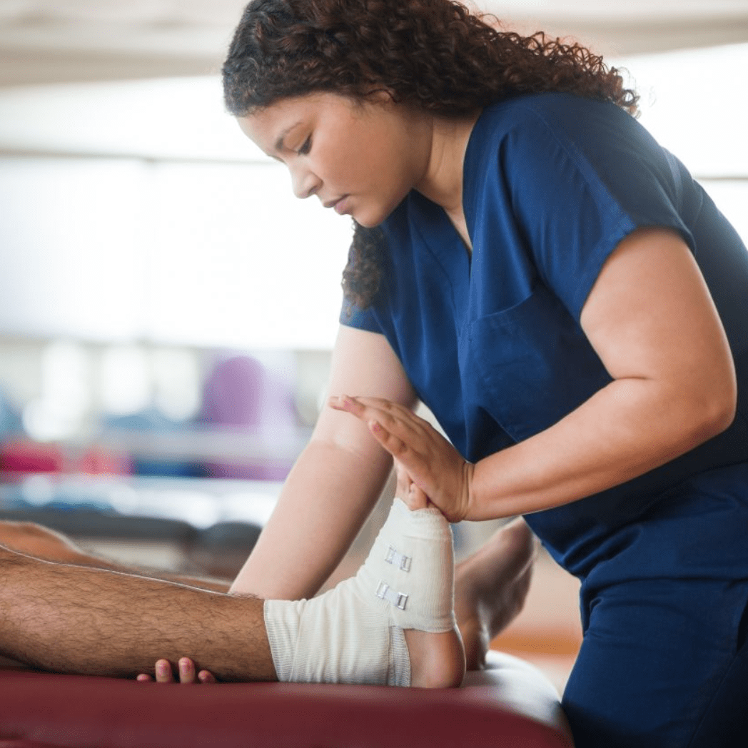 Una fisioterapeuta ejercita el pie y el tobillo lesionados de un hombre tumbado en una camilla.