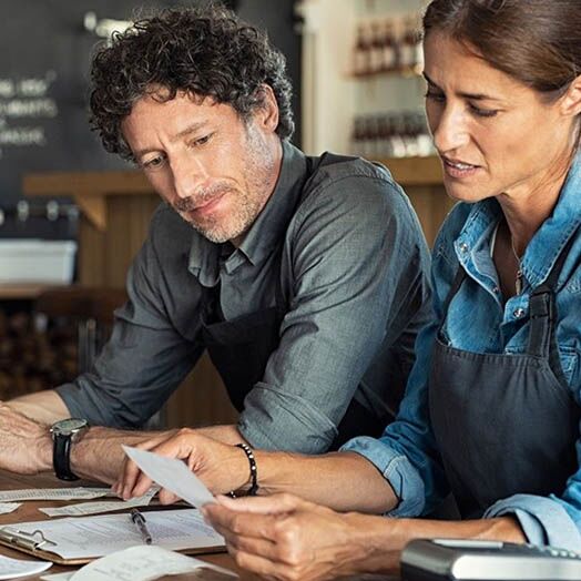 Un hombre y una mujer propietarios de pequeñas empresas revisando papeleo.