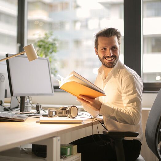 Hombre sonriente sentado ante un escritorio y sosteniendo un libro amarillo.
