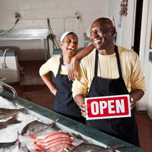 Un hombre y una mujer en un mercado de pescado sonriendo y sosteniendo un cartel abierto para negocios.