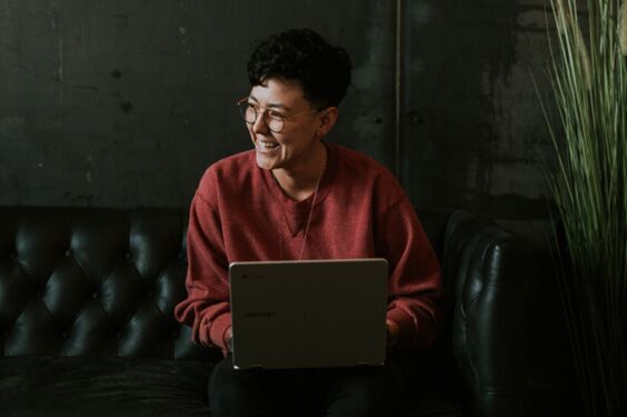 Mujer sonriente trabajando en una laptop sentada en un sofá de cuero negro.