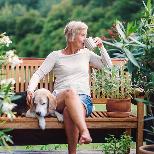 Mujer mayor tomando café en el porche mientras acaricia a su perro.