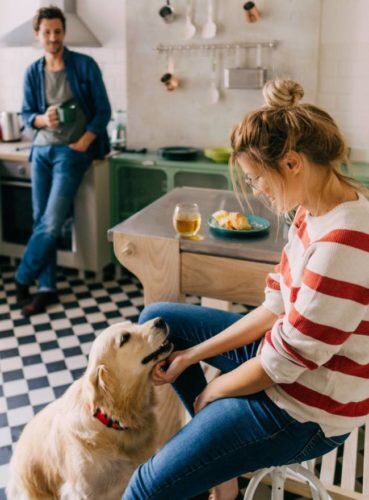Woman playing with dog in kitchen as man watches