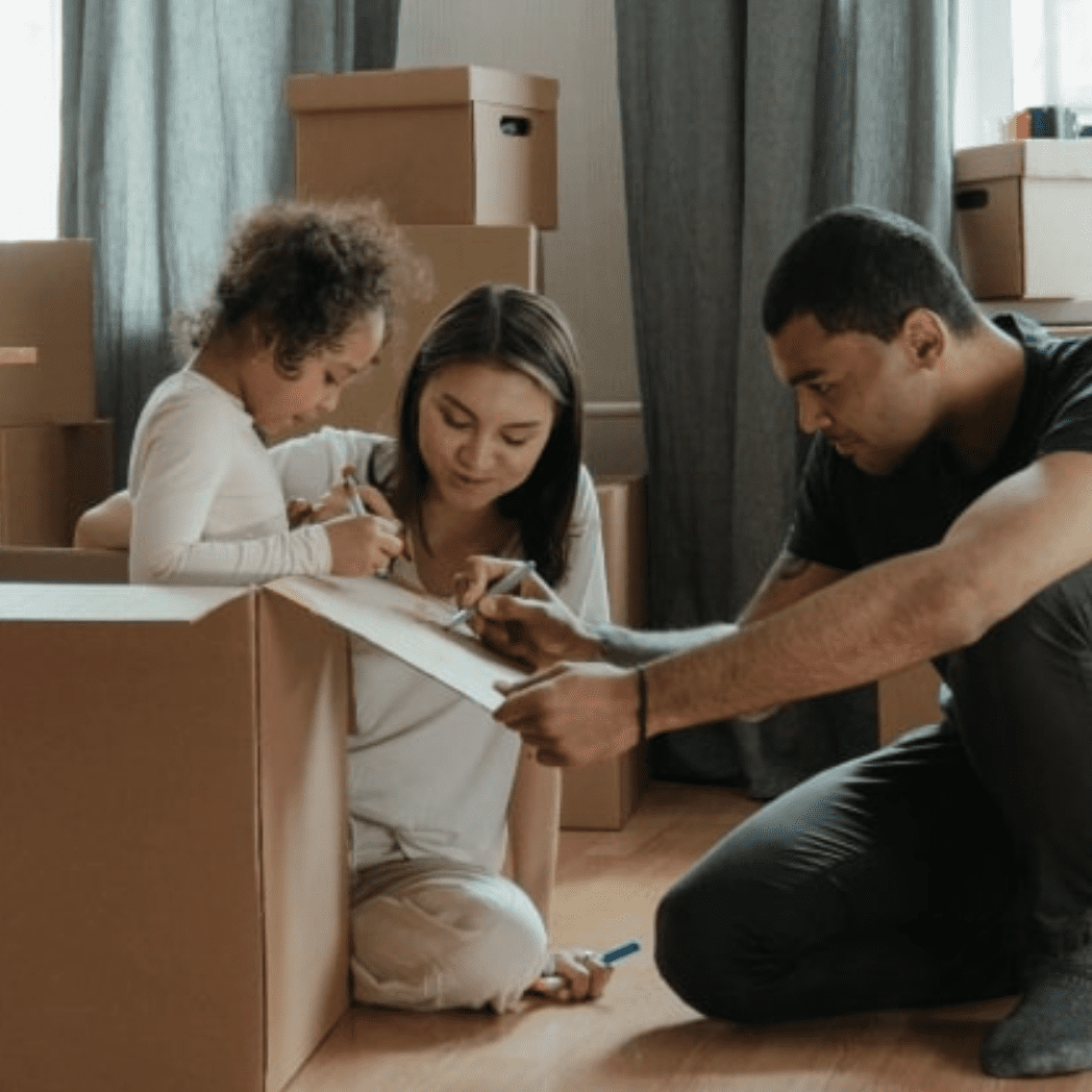 Una madre, un padre y una niña etiquetando cajas de mudanza