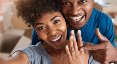 Smiling young couple with woman showing her engagement ring.