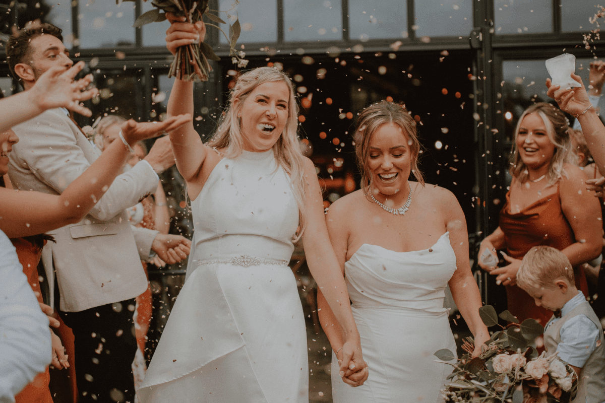 2 brides leaving their marriage ceremony in celebration as confetti is being thrown at them.
