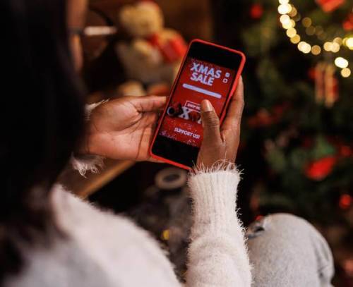 Woman looking at her phone with Xmas Sale Support Us text on screen.