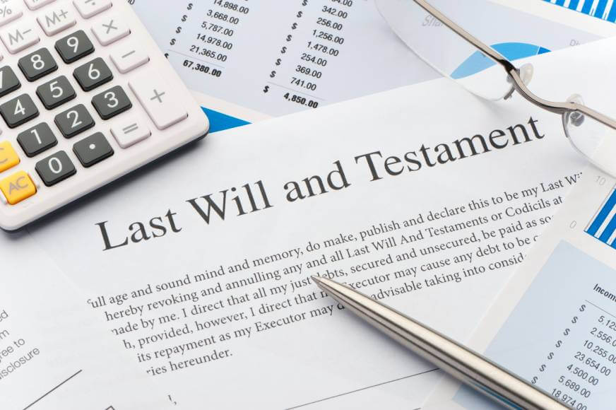 Last Will and Testament on a desk next to a calculator, ink pen and eyeglasses.