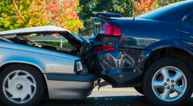 Rear end car crash between a grey and blue car.