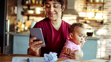 Mother holding a baby and looking at her cellphone.